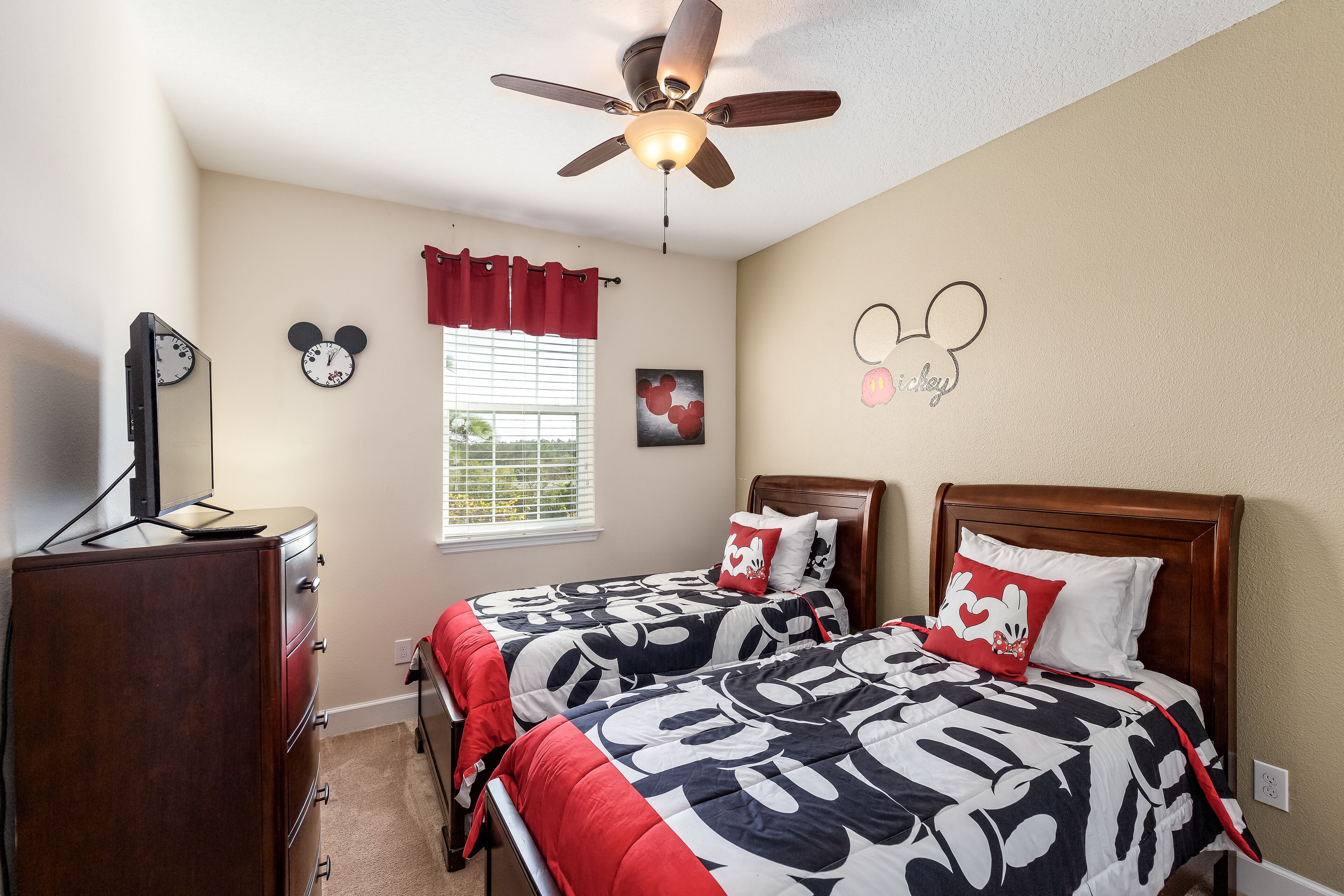Ein Schlafzimmer mit zwei Betten, einem Deckenventilator, einer Kommode und Mickey Mouse Dekoration.