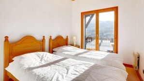 Ein Schlafzimmer mit zwei hölzernen Betten, einem großen Fenster mit Bergblick und einer Holzbalkendecke.