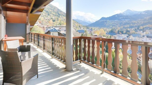 Ein Balkon mit Korbmöbeln, Blick auf eine Stadt und Berge.