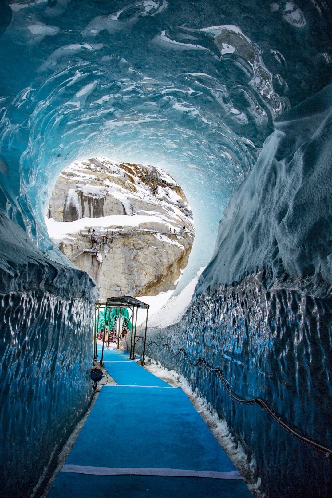 An ice tunnel with a clear view of a snow-covered rock formation at the end.