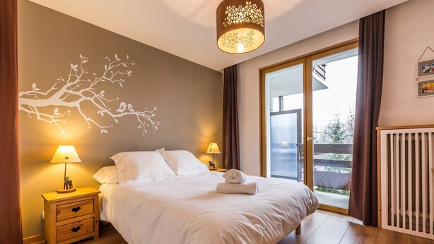 Ein Schlafzimmer mit einem Bett, zwei Nachttischen mit Lampen, Wandgemälde und Blick durch eine Glastür.