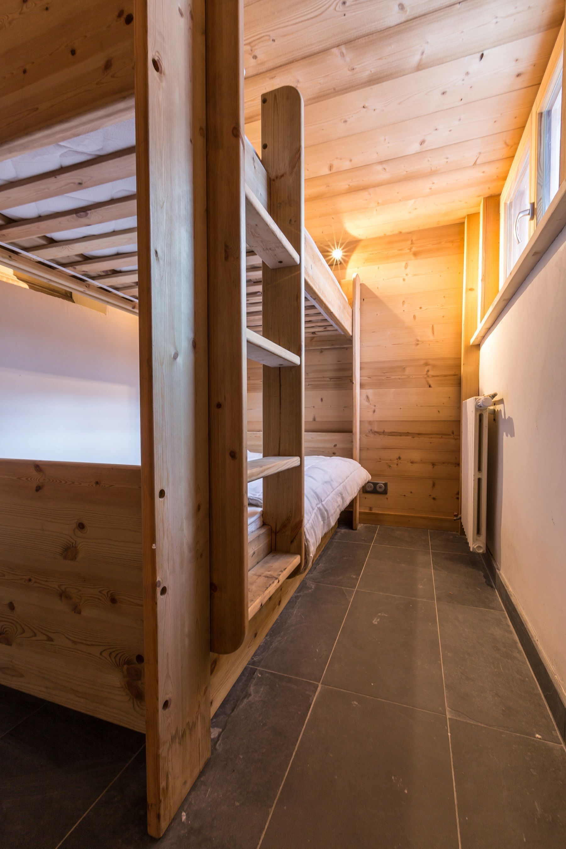 Quarto de madeira pequeno com beliches e radiador.