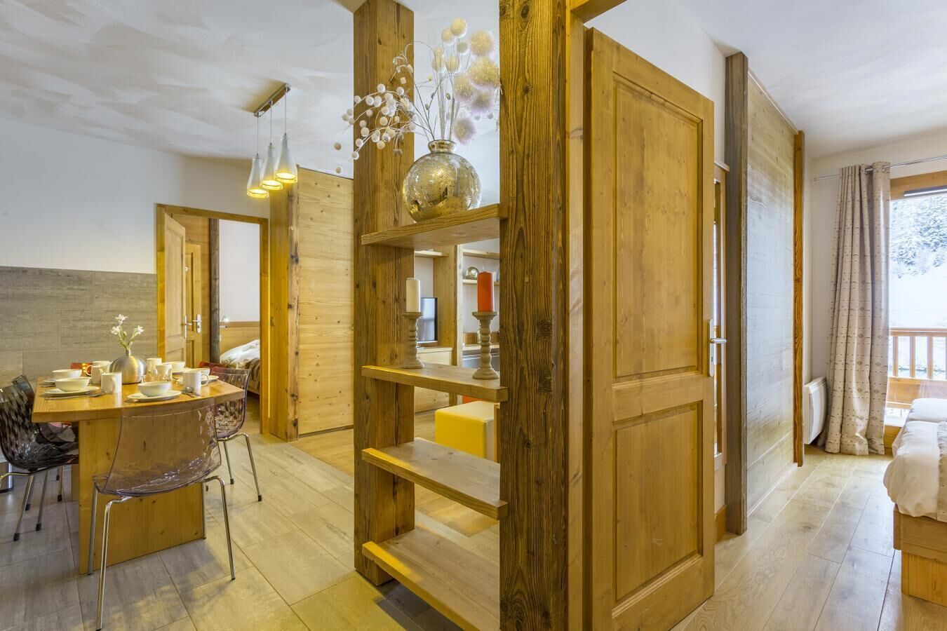 A modern interior with a wooden dining area, a built-in shelf with decorative items, and a cozy seating area with a view of the outdoors.