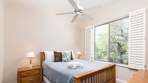 A bedroom with a bed, nightstands, a ceiling fan, a window with shutters, and a view of trees. - Reduced Rates Just Posted! Cachet Condo (Scottsdale)