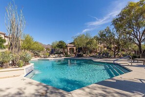 A swimming pool with lounge chairs and a pergola, surrounded by desert vegetation and buildings. - Reduced Rates Just Posted! Cachet Condo (Scottsdale)