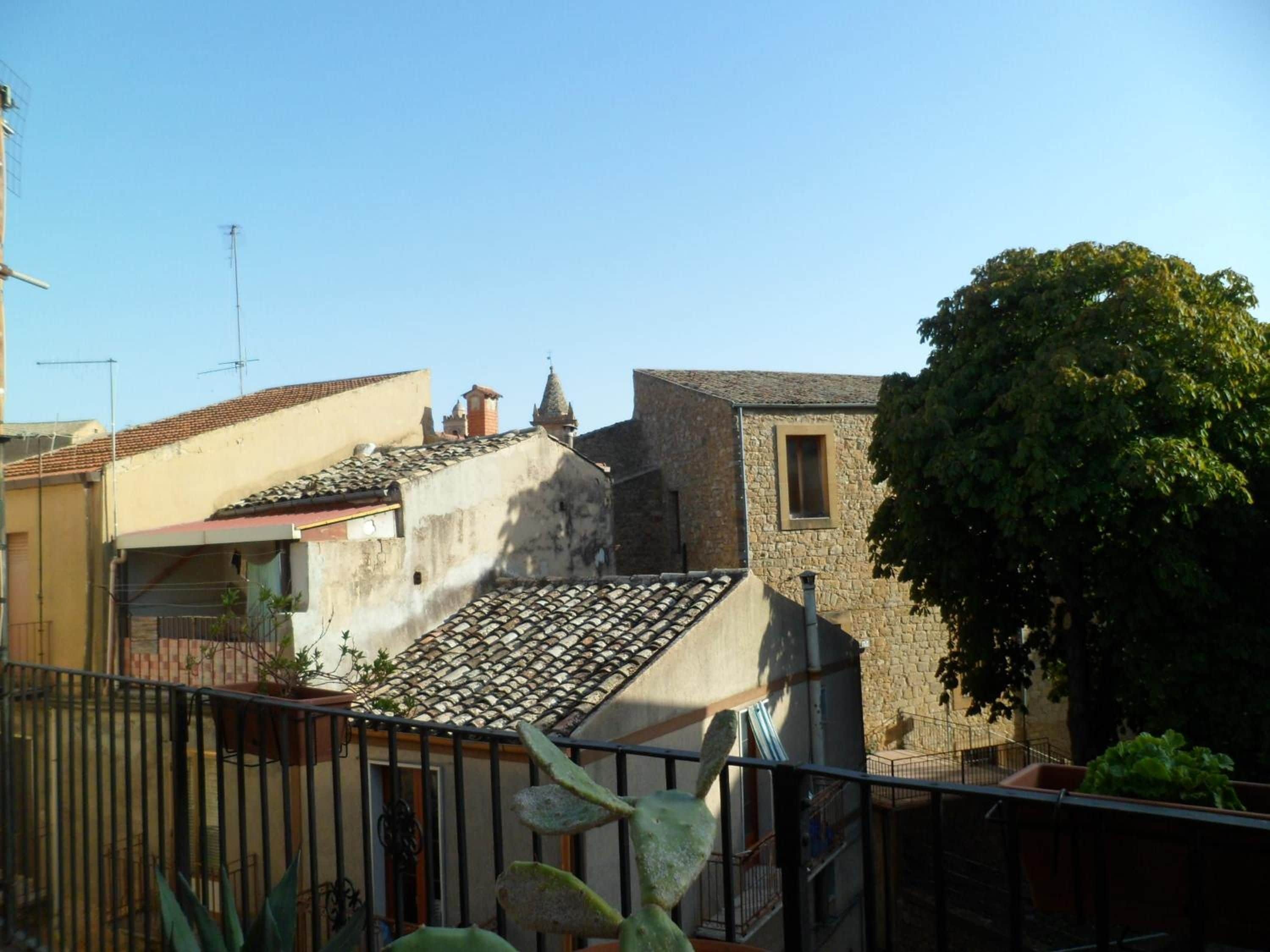 Zona residencial com edifícios de pedra, telhado de telhas e uma grande árvore.
