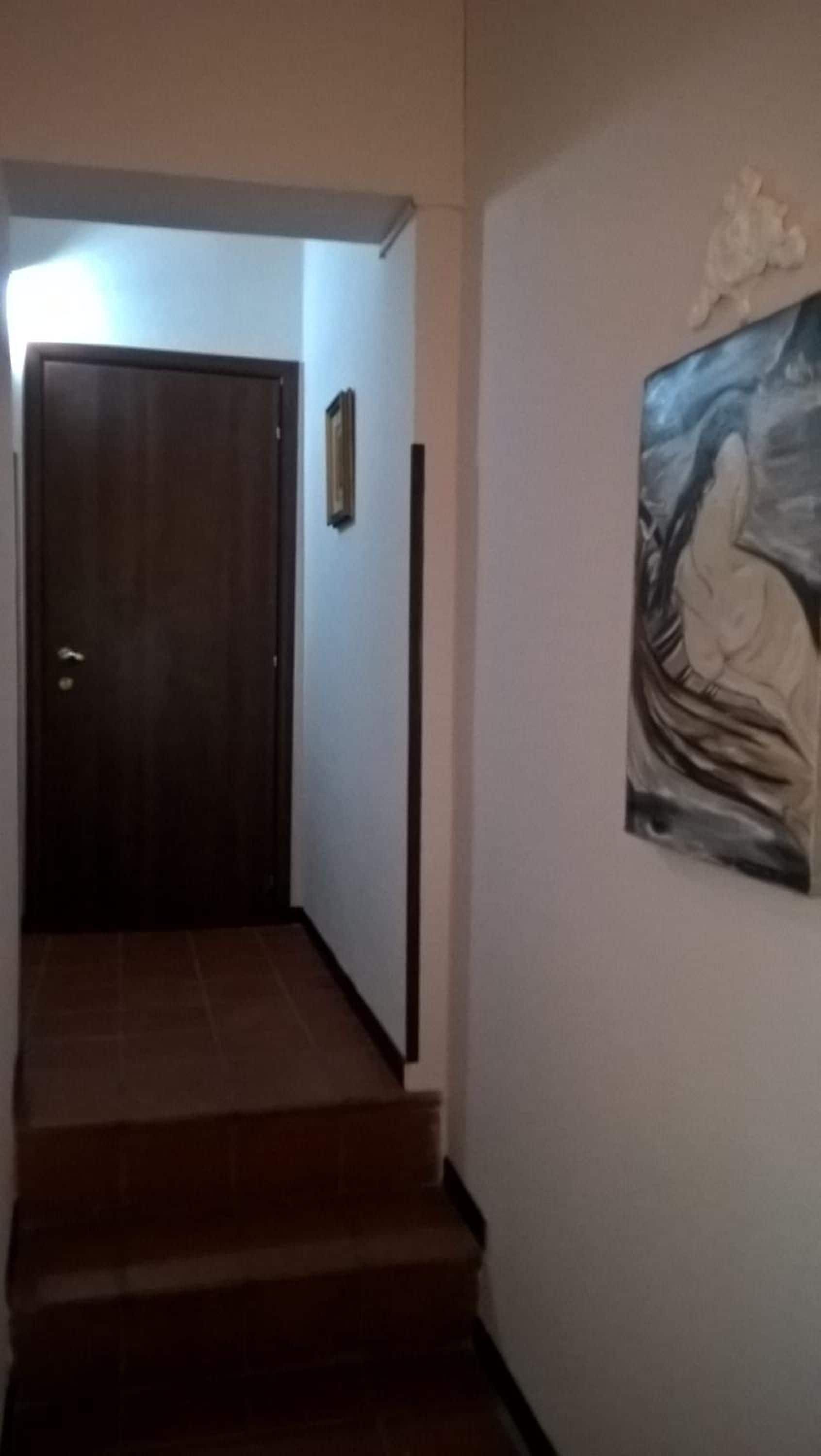 A staircase leading to a dark wooden door, a framed picture on the wall, and a painting above the door.