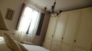 A bedroom with a bed, a chandelier, a wardrobe, and a window with curtains. - La Dea Bendata (Piazza Armerina)