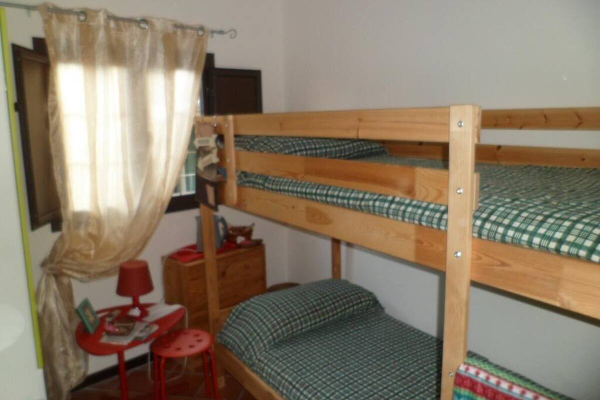 Habitación con literas, una pequeña mesa, una silla, una lámpara roja y una cortina.
