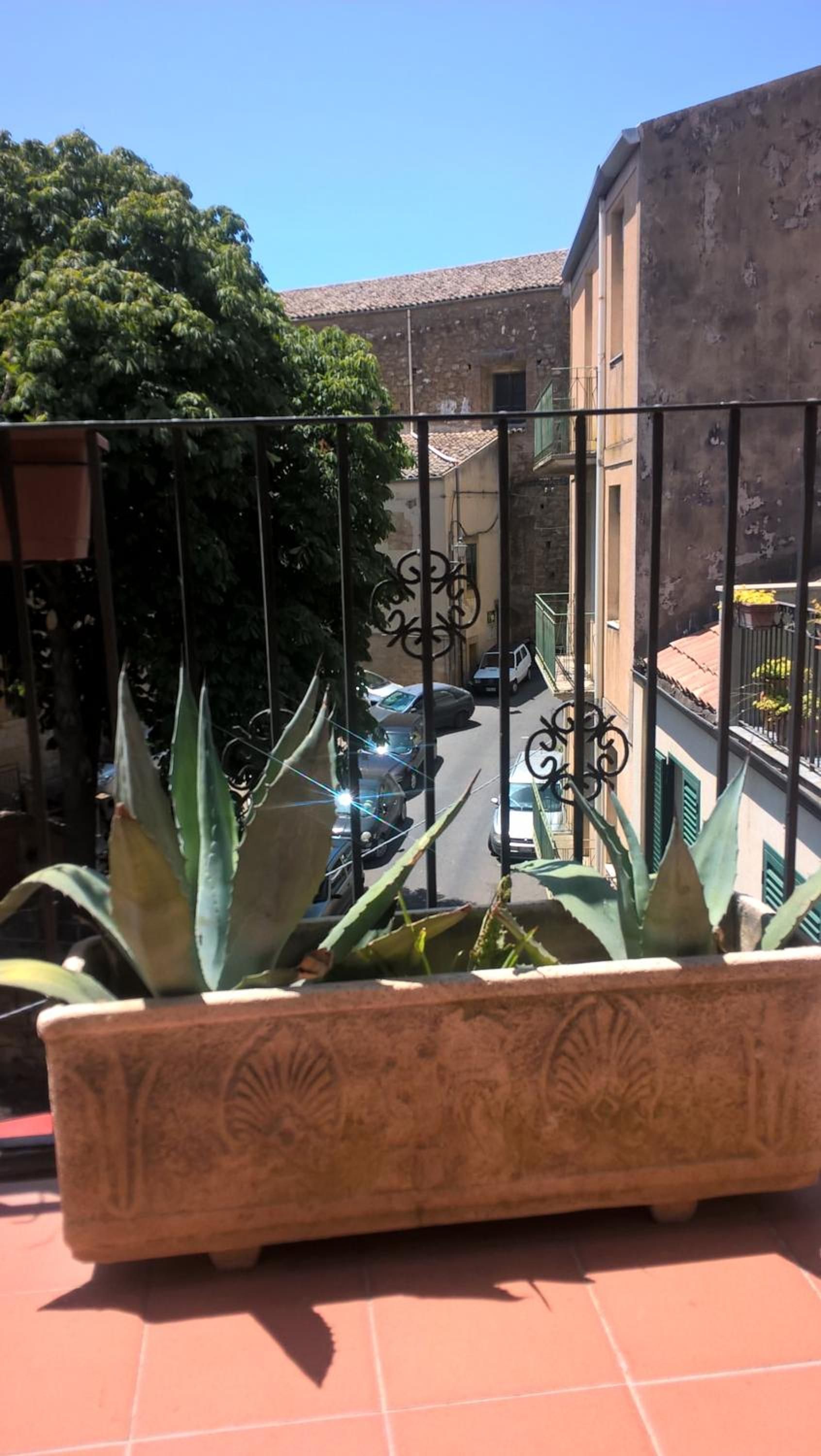 Uma varanda com vista para a rua, um vaso de planta e um edifício com telhado de azulejos.