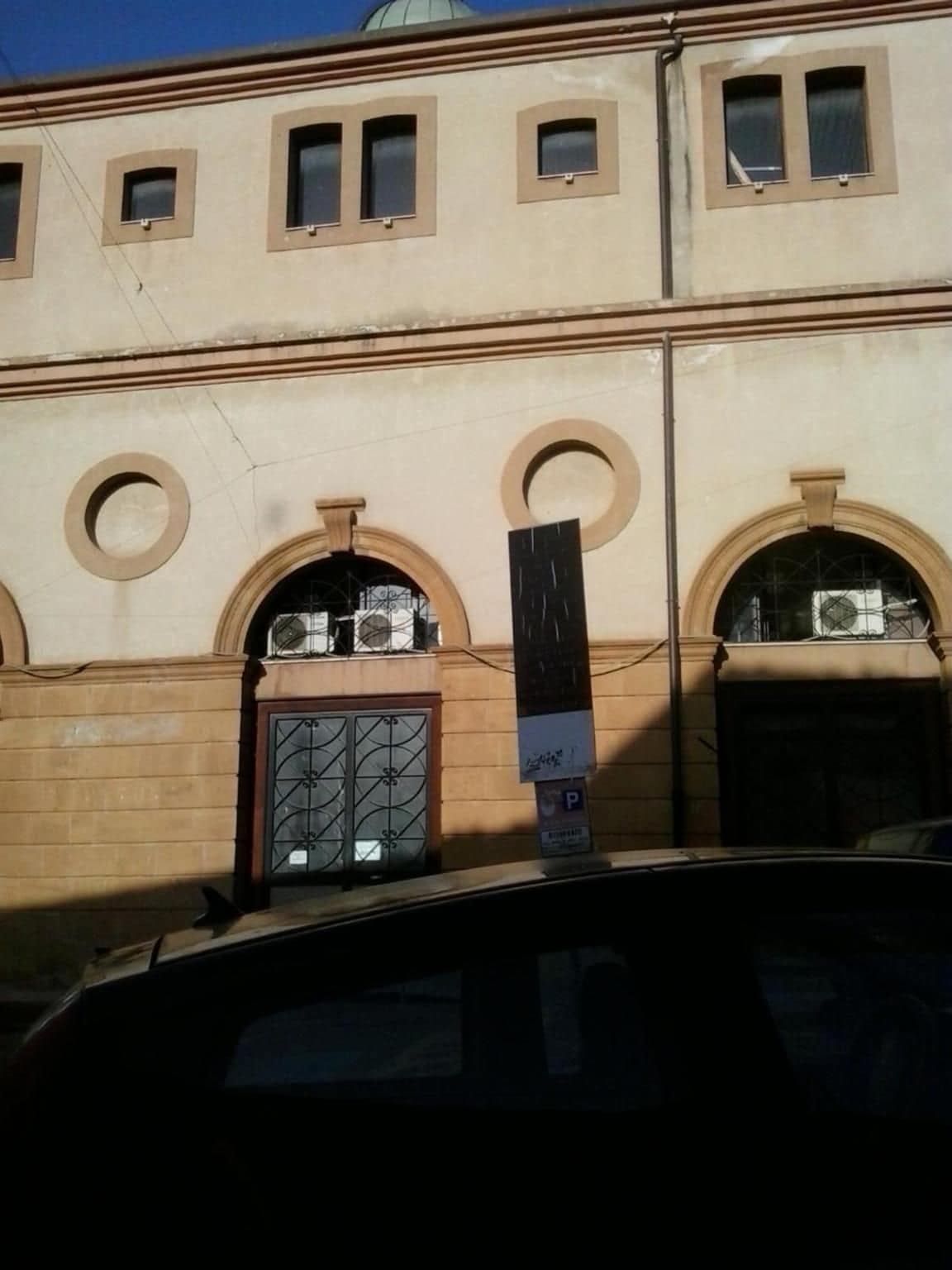 Un edificio con varias ventanas, una puerta central con celosía decorativa y un letrero de estacionamiento.
