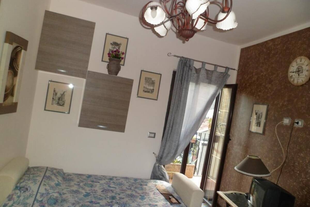 Un dormitorio con cama, escritorio con computadora, candelabro y reloj en la pared.