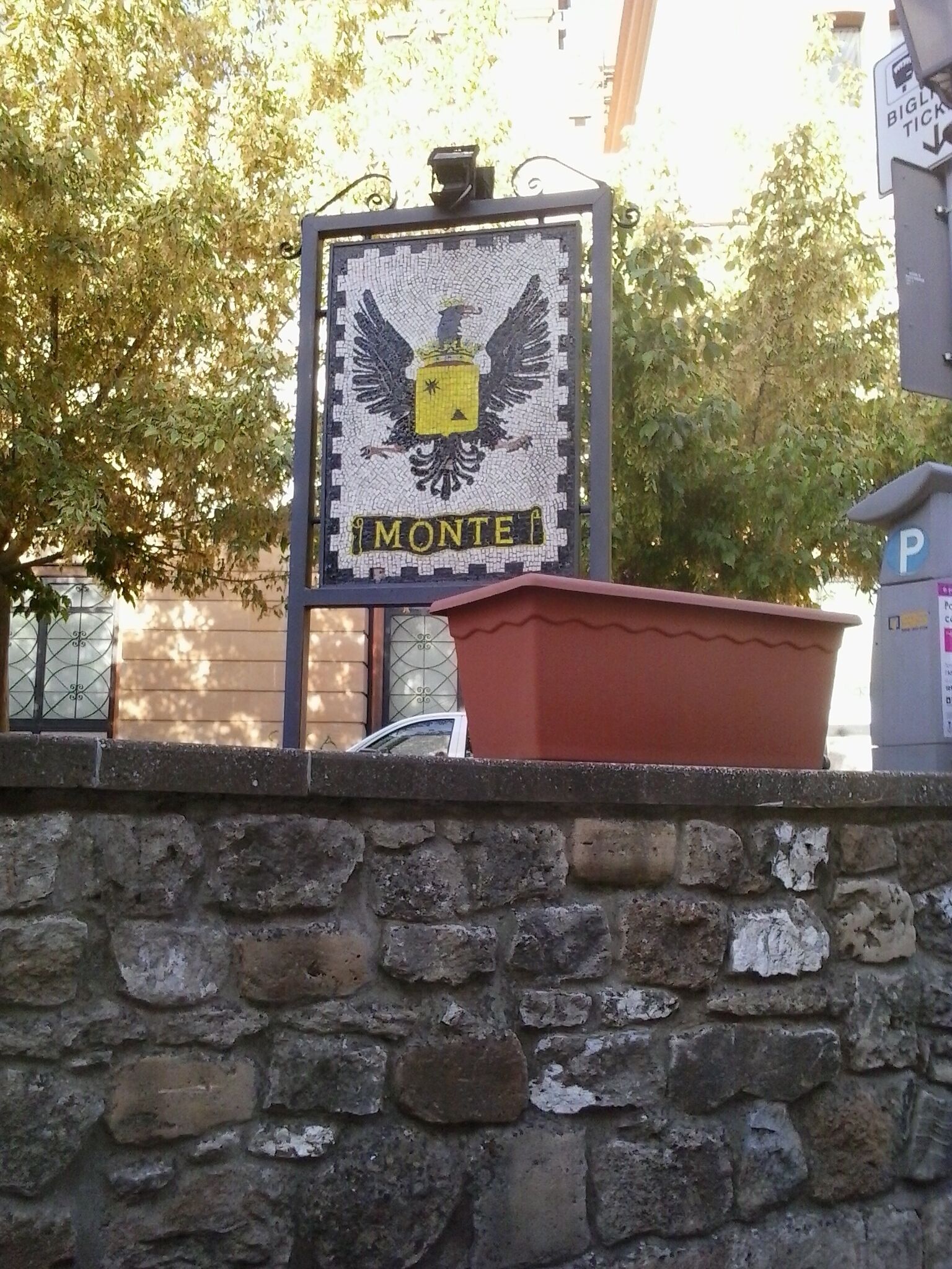 Ein Schild mit Adlerwappen und dem Wort 'MONTE' an einer Steinmauer.