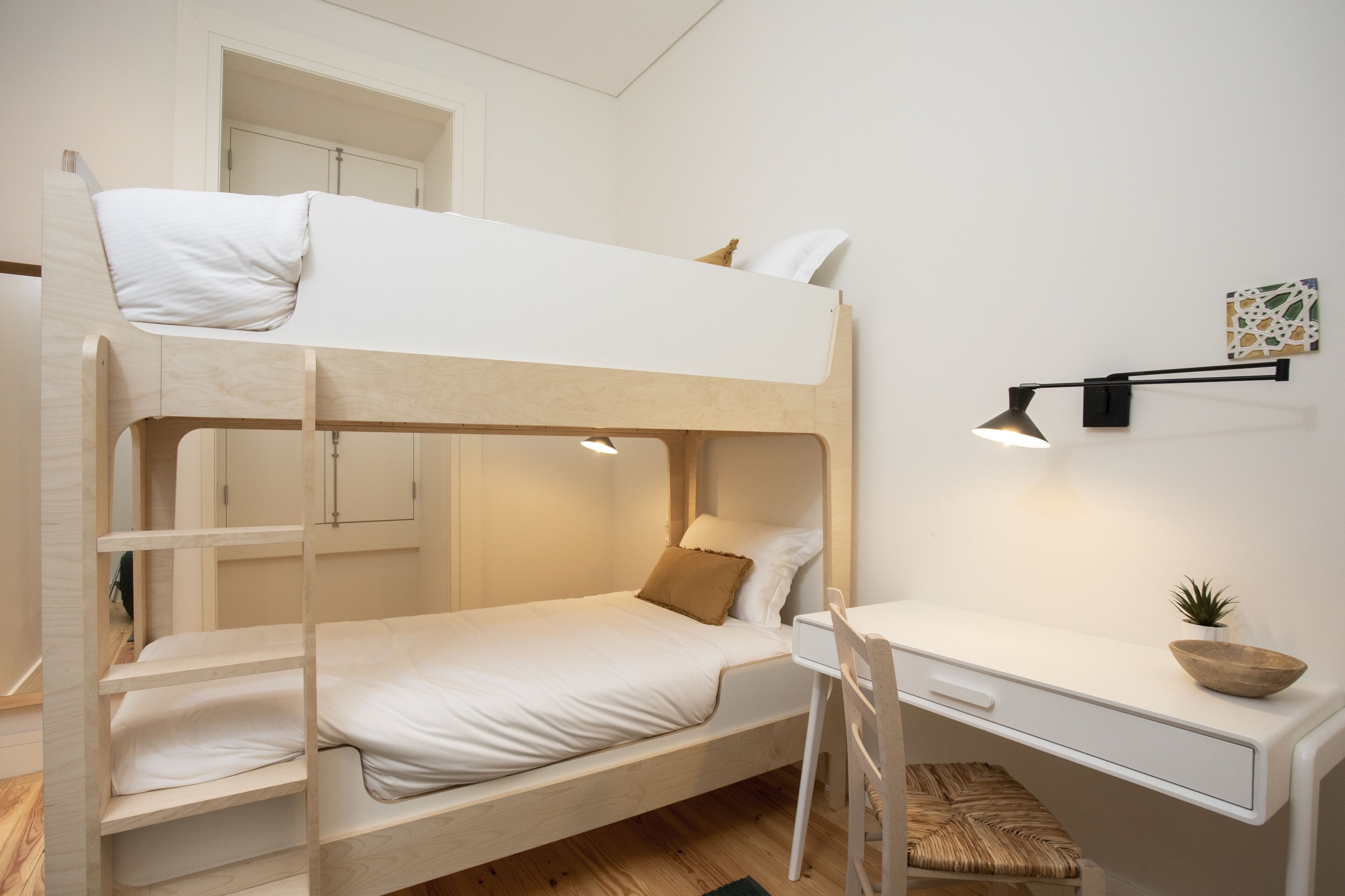 Habitación con literas, escritorio, silla, una planta pequeña y una lámpara de pared.