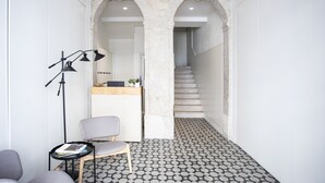 A hallway with a patterned floor, a reception desk, a chair, and a desk lamp. - Montebelo Lisbon Downtown Apartments (Lisbon)