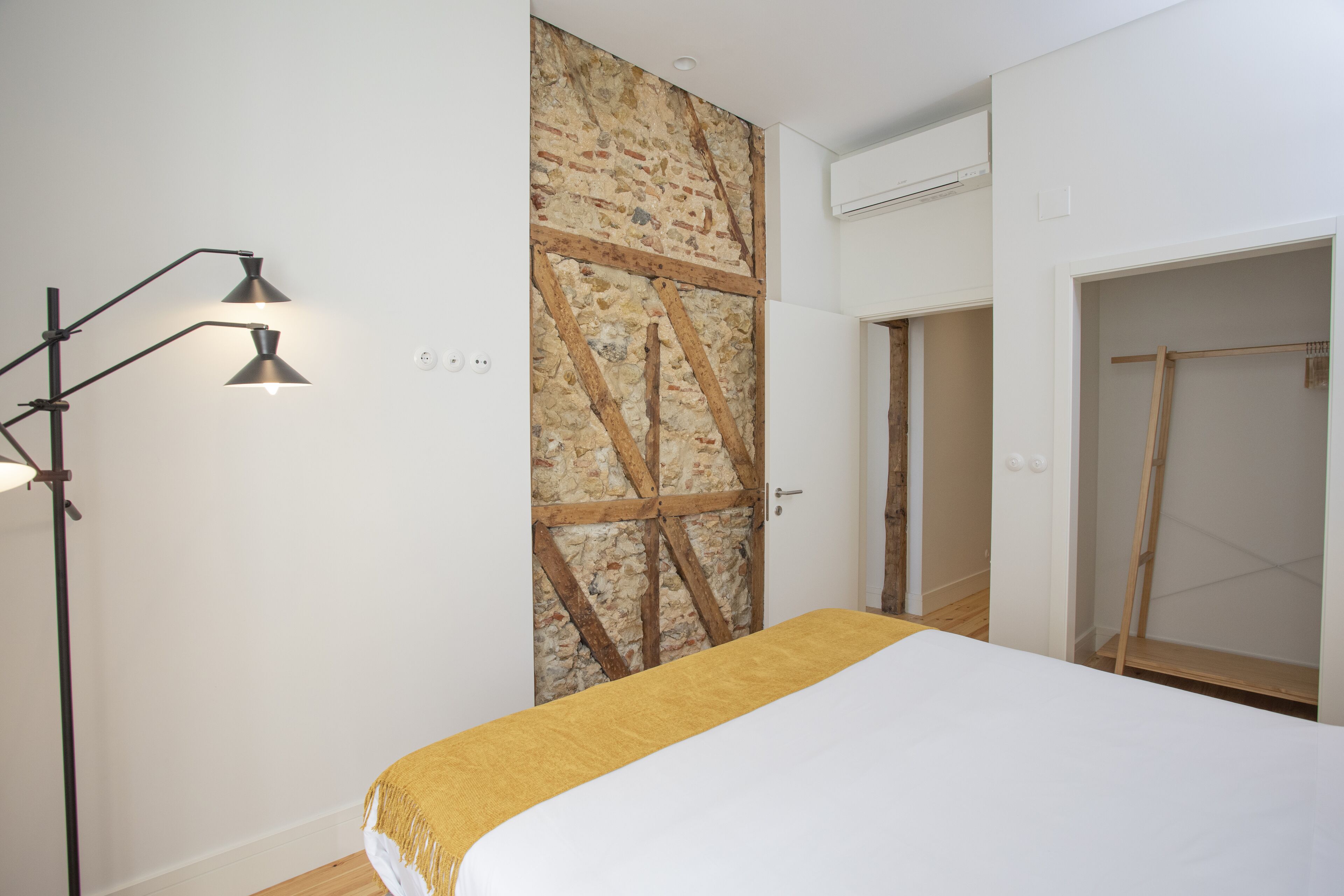 A bedroom with a bed, a wardrobe, a door with a stone wall, and a floor lamp.