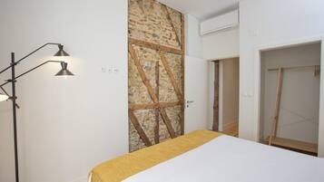 A bedroom with a bed, a wardrobe, a door with a stone wall, and a floor lamp.