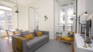 A modern living room with a grey sofa, yellow cushions, a patterned rug, and a dining area with a table and chairs. - Montebelo Lisbon Downtown Apartments (Lisbon)