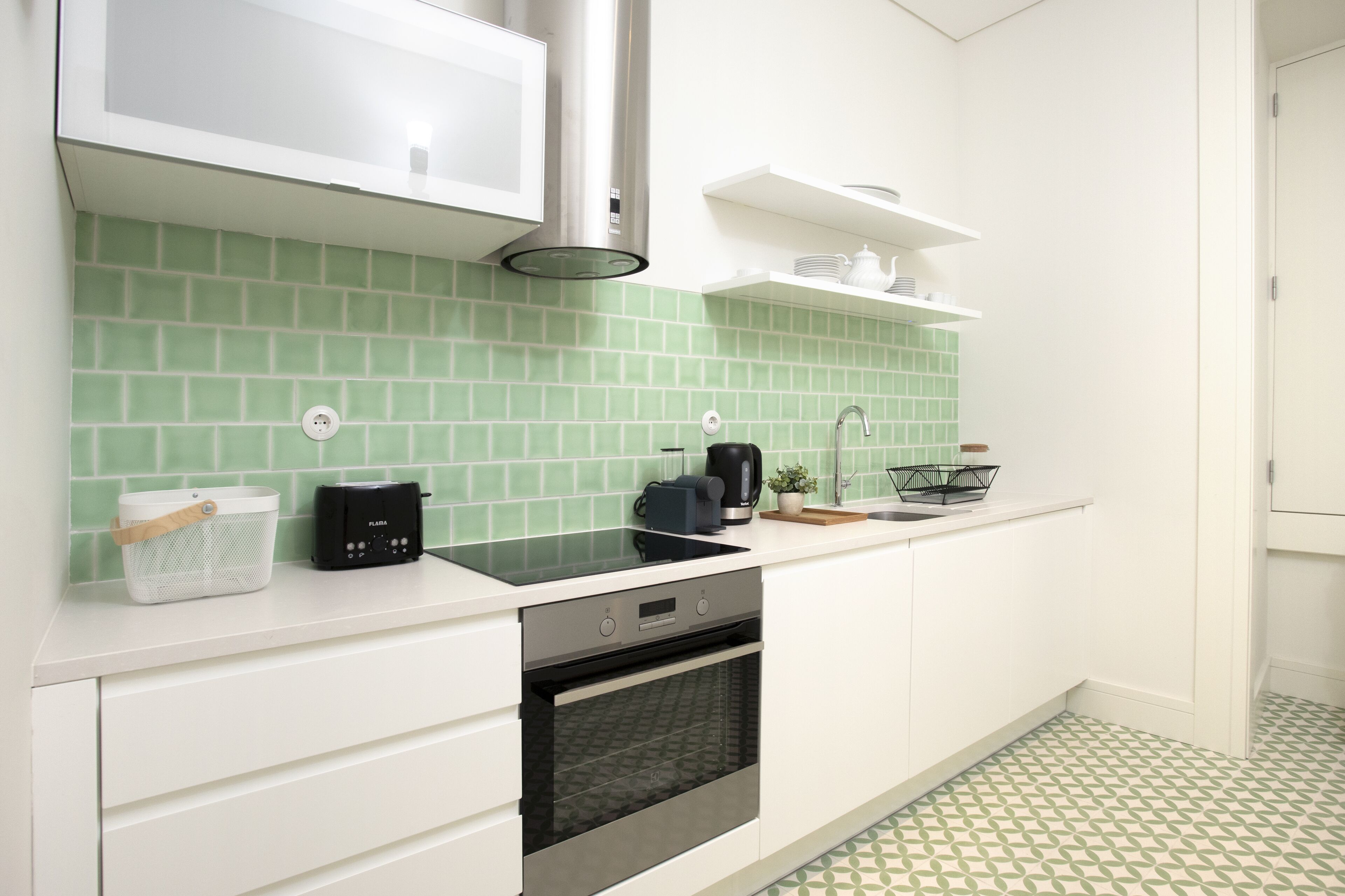 A modern kitchen with white cabinets, a black stove, and a green tiled backsplash.