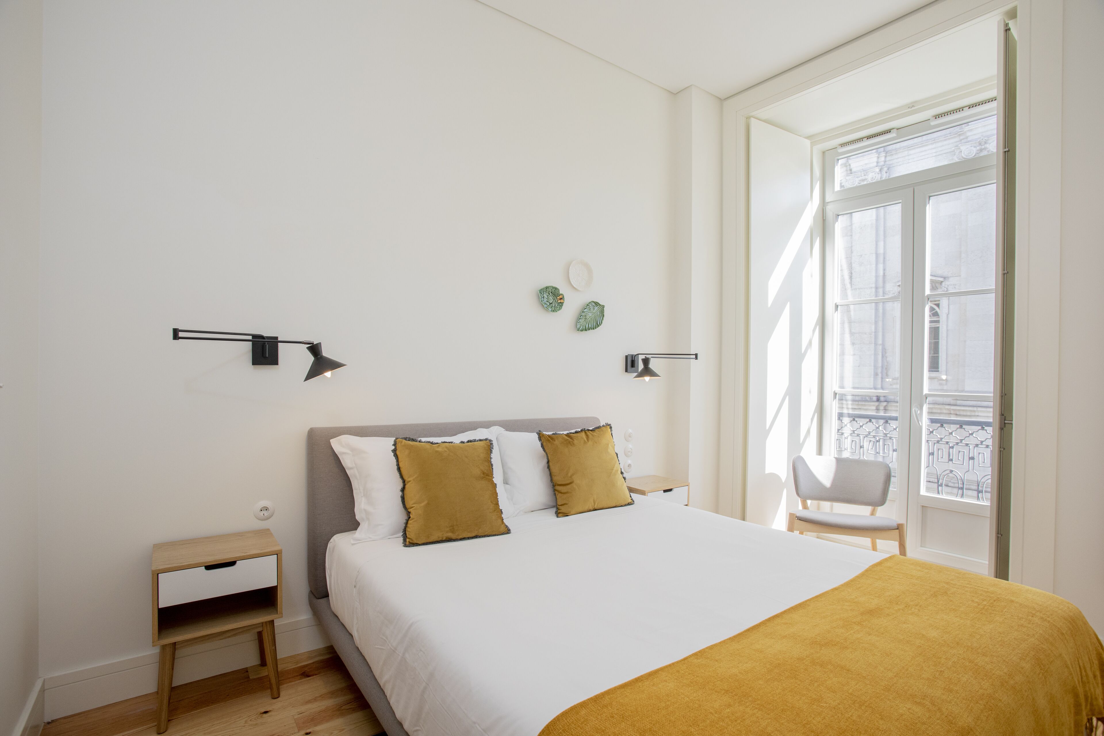 Quarto com cama, mesas de cabeceira e janela com vista para uma varanda.