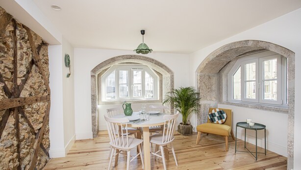 A dining area with a wooden table and chairs, a potted plant, and a chair with a checkered cushion. - Montebelo Lisbon Downtown Apartments (Lisbon)