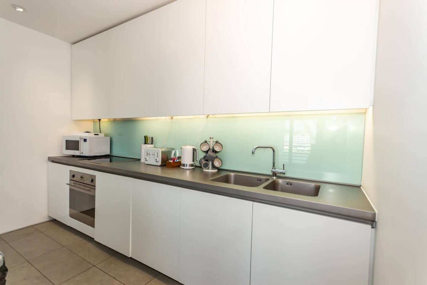 A modern kitchen with white cabinets, a stainless steel countertop, a microwave, a toaster, and a sink.