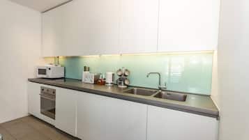 A modern kitchen with white cabinets, a stainless steel countertop, a microwave, a toaster, and a sink.