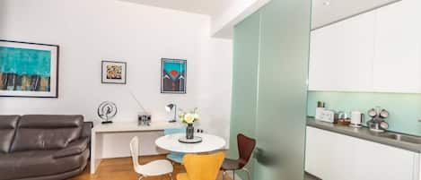 A modern living room with a sofa, a dining table with chairs, and a kitchen area with cabinets and appliances.
