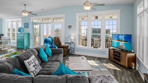 A spacious living room with a gray sofa, teal cushions, a wooden coffee table, and a television on a wooden stand. - "A Penny From Heaven" 2nd row luxury 4 bedroom with pool (Holden Beach)