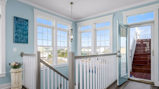 A spacious room with large windows, a white railing, and a staircase leading to a deck. - "A Penny From Heaven" 2nd row luxury 4 bedroom with pool (Holden Beach)