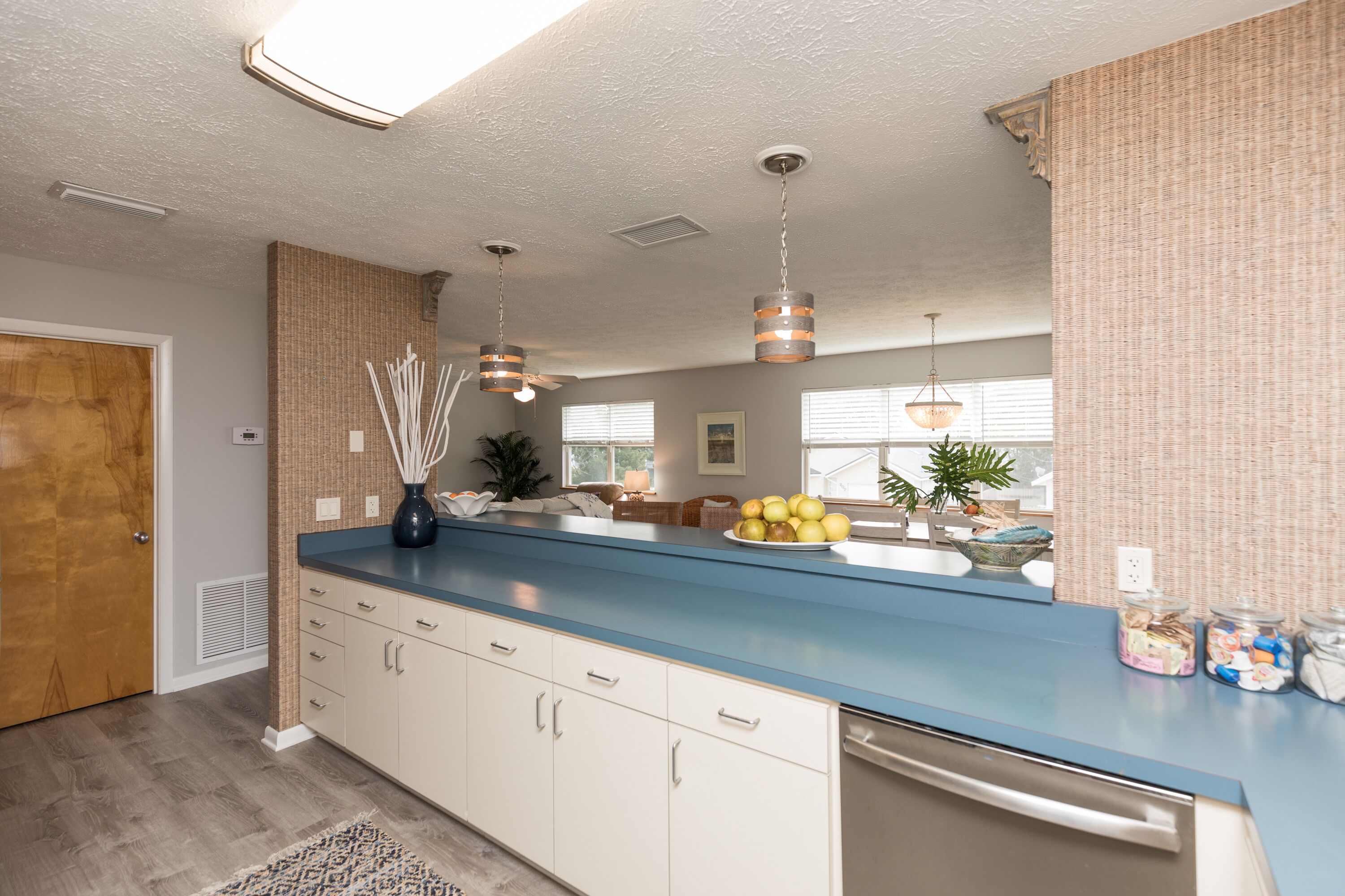 Een keuken met een blauw aanrecht, witte kasten en hangende pendelverlichting.