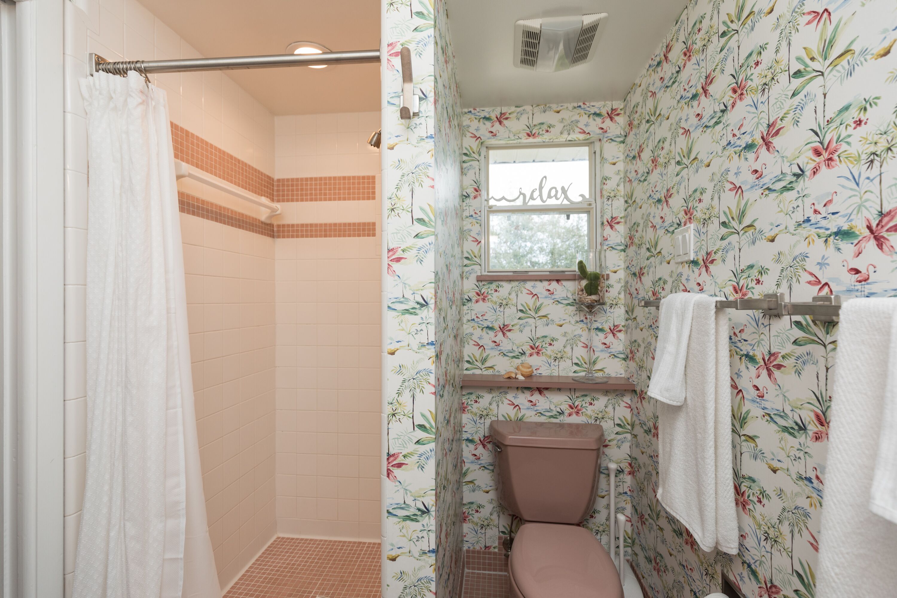 A bathroom with a shower, toilet, and a window with a floral wallpaper.
