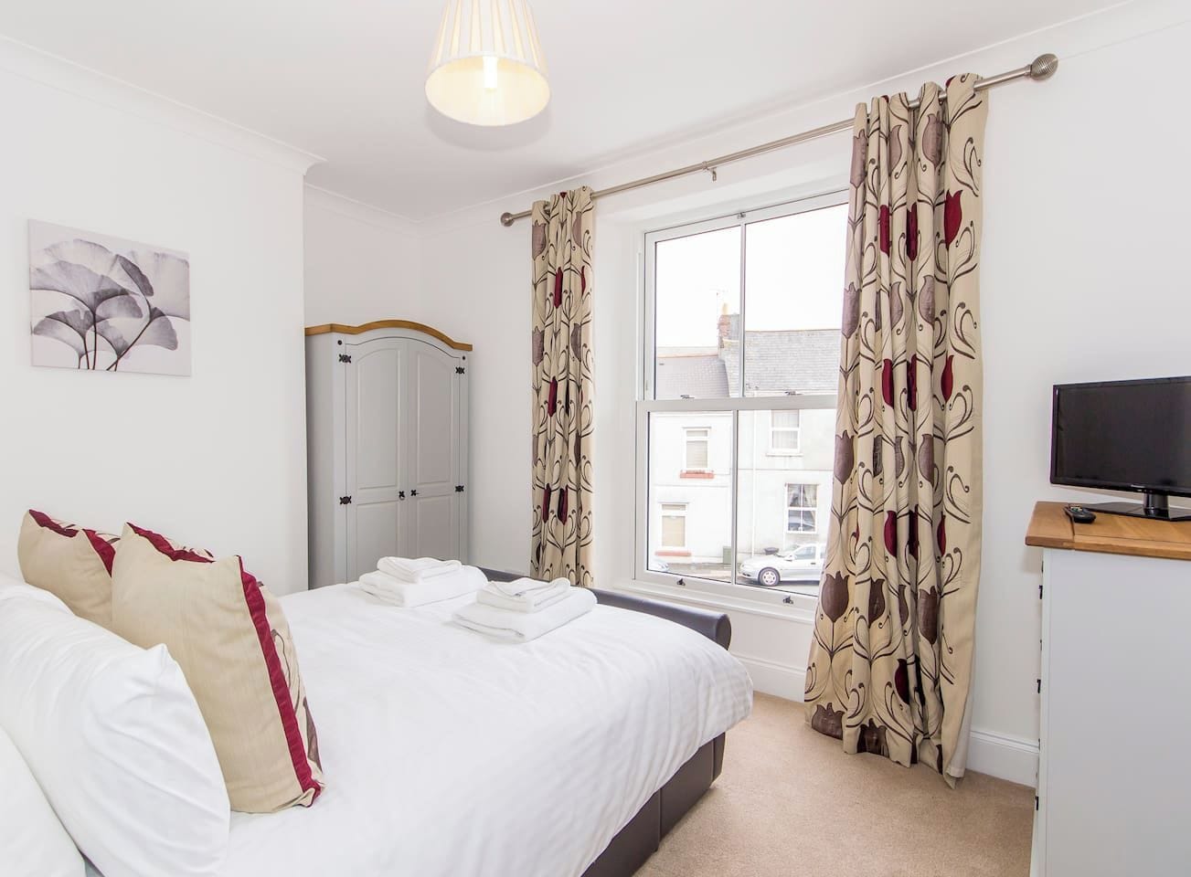 A hotel room with a bed, a television, a wardrobe, and a window with curtains.