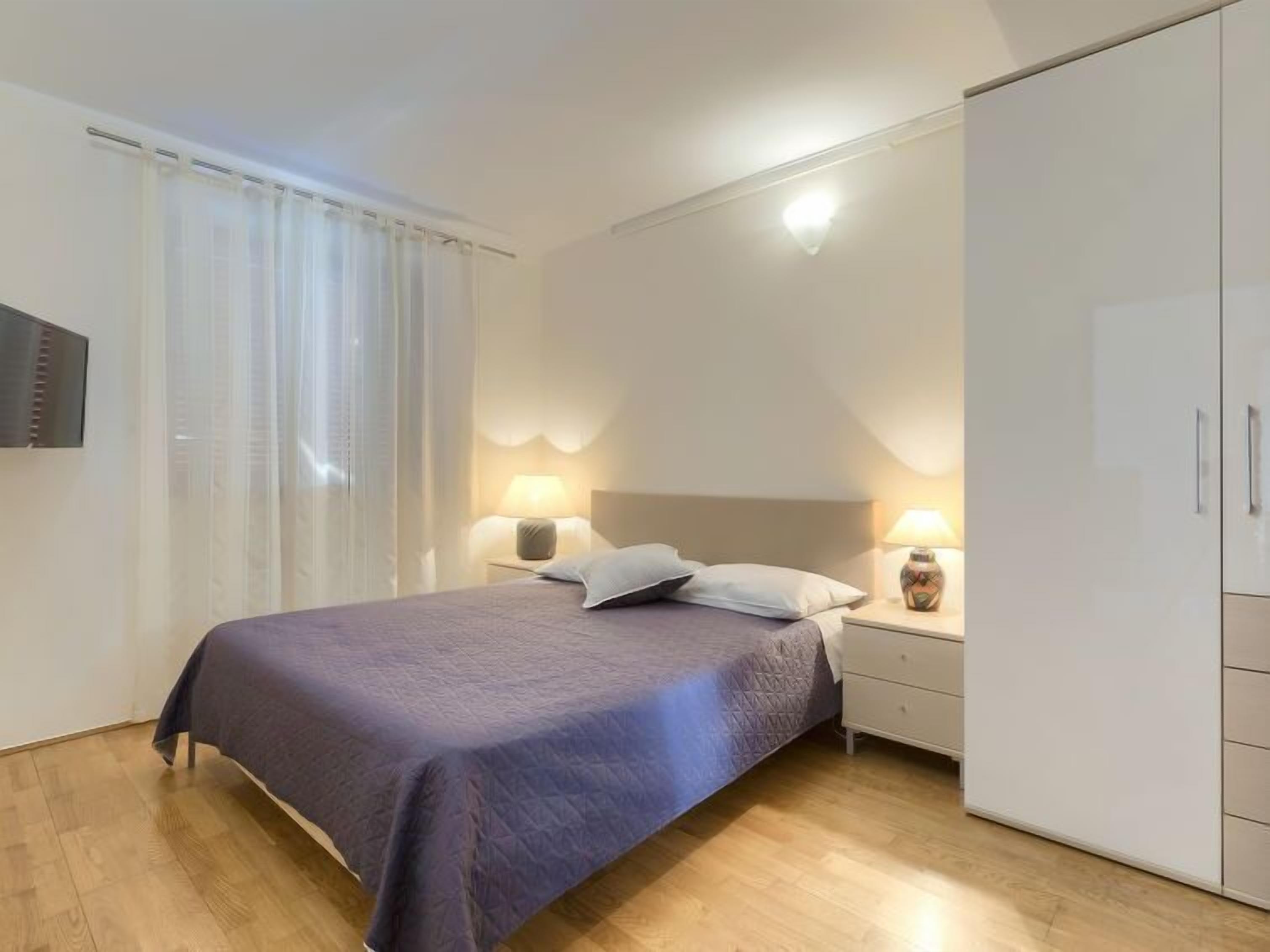 A bedroom with a bed, bedside lamps, a wardrobe, and a window with curtains.
