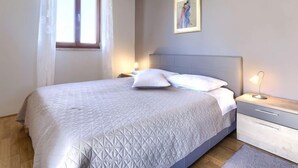 Un dormitorio con cama, mesitas de noche, aire acondicionado, una ventana con cortinas y un cuadro en la pared.