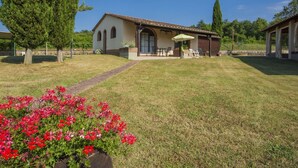 A house with a patio, a lawn, and a garden with red flowers. - Cosy apartment in villa for 7 people with pool, WIFI, TV and pets allowed (Bucine)