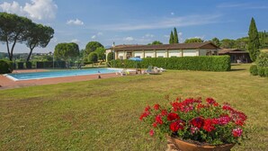 A pool area with a clear sky, a building with a tiled roof, and a flower bed with red flowers. - Cosy apartment in villa for 7 people with pool, WIFI, TV and pets allowed (Bucine)