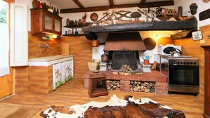 A rustic kitchen with a brick fireplace, wooden beams, and a stone wall.