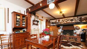 A rustic dining area with a wooden table and chairs, a brick fireplace, and a cowhide rug.