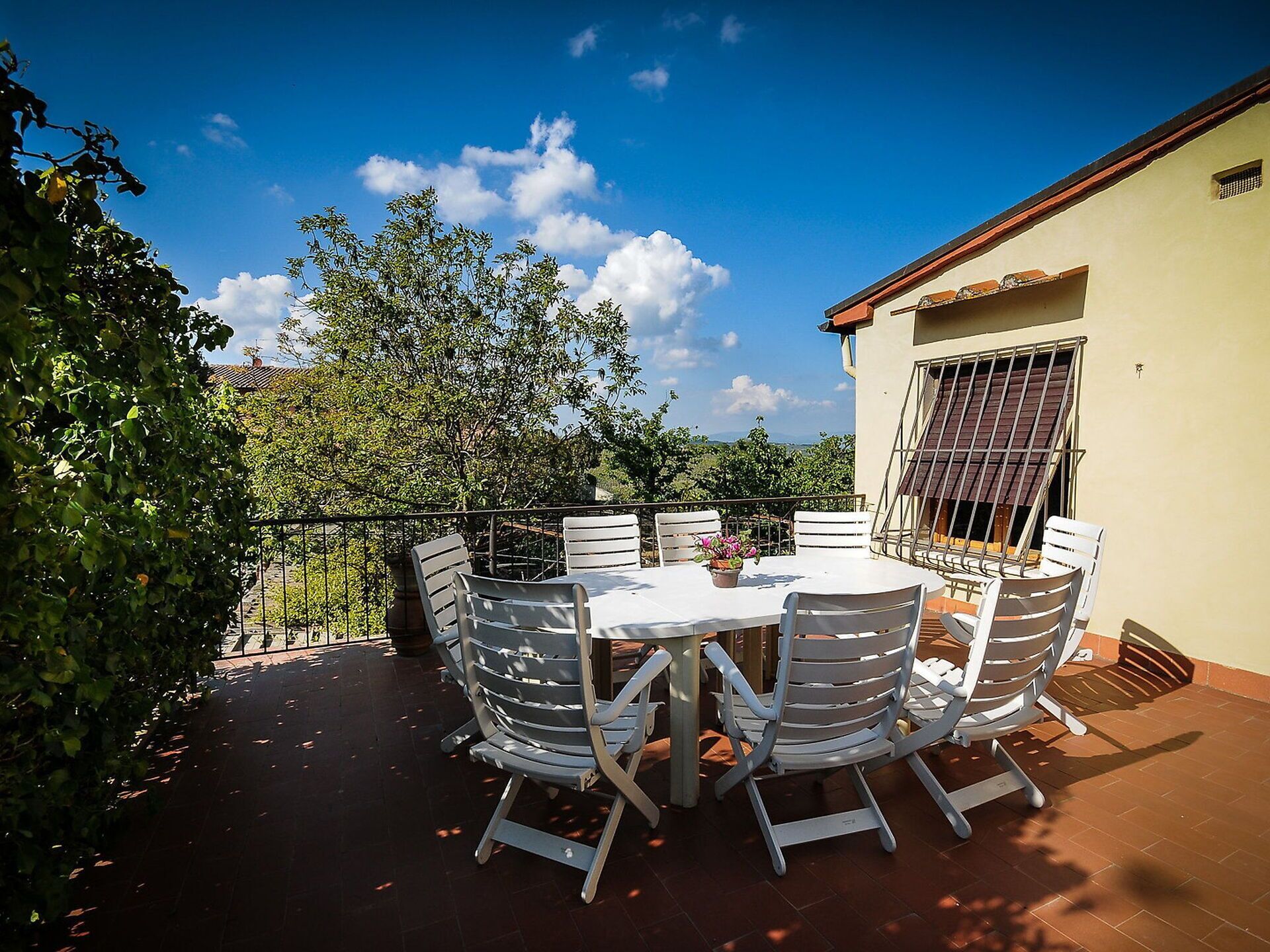 Une terrasse avec une table ronde et six chaises, entourée d’une rambarde en métal.