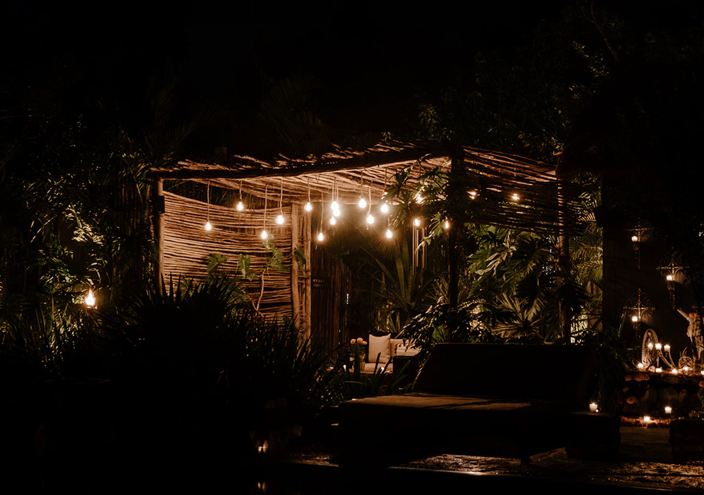 An outdoor seating area with string lights and a small table, surrounded by lush greenery.