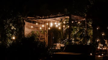 An outdoor seating area with string lights and a small table, surrounded by lush greenery.