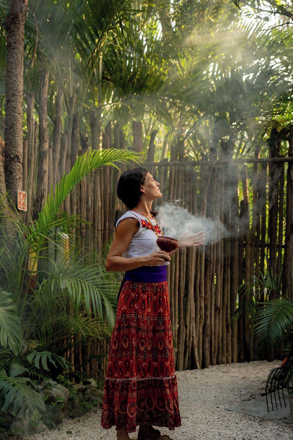A person in a patterned dress standing in a garden with bamboo fencing and tropical plants.