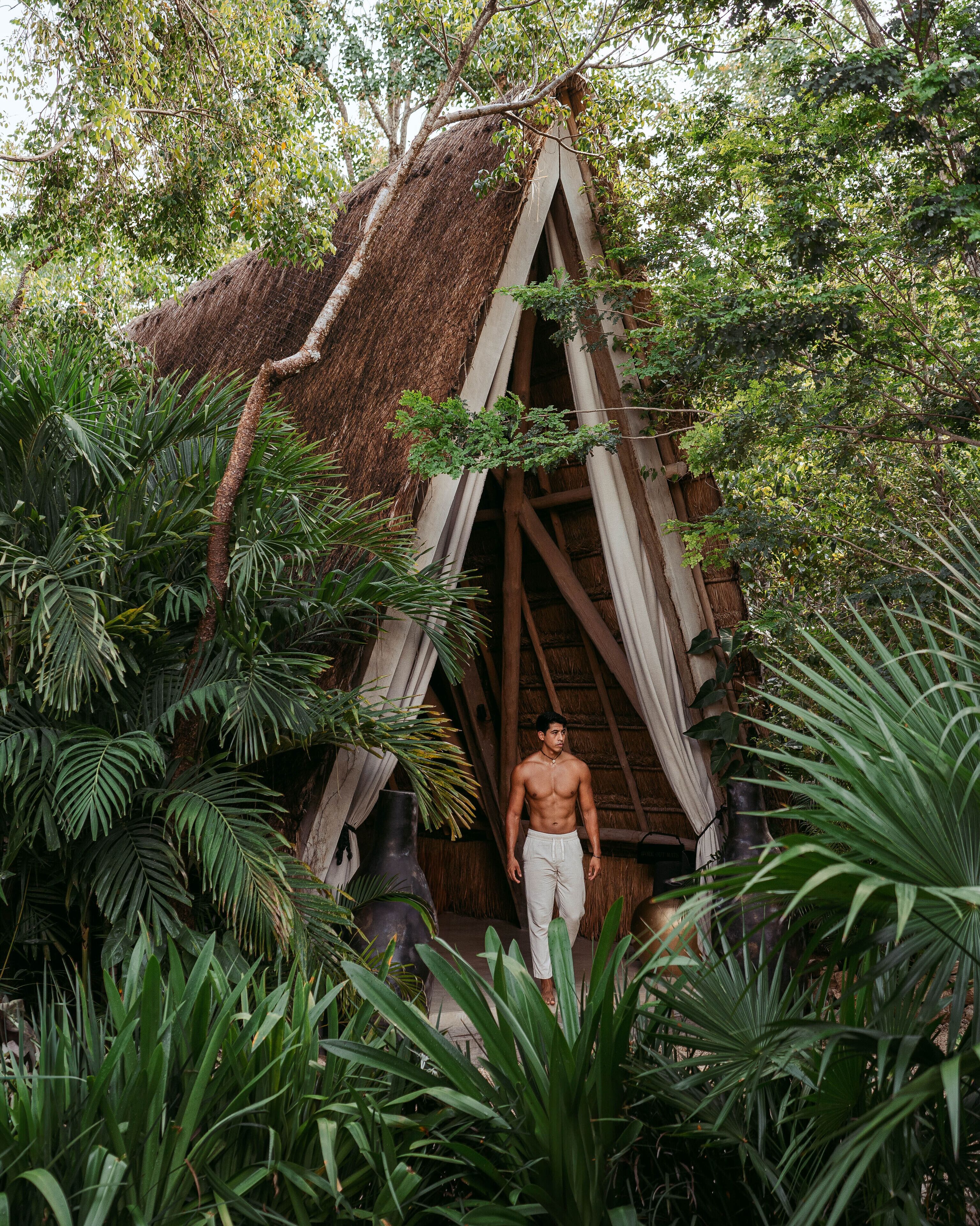 A man standing in front of a thatched-roof structure surrounded by lush greenery.