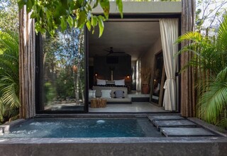 A modern outdoor bedroom with a glass door, a small pool, and a sofa with pillows.