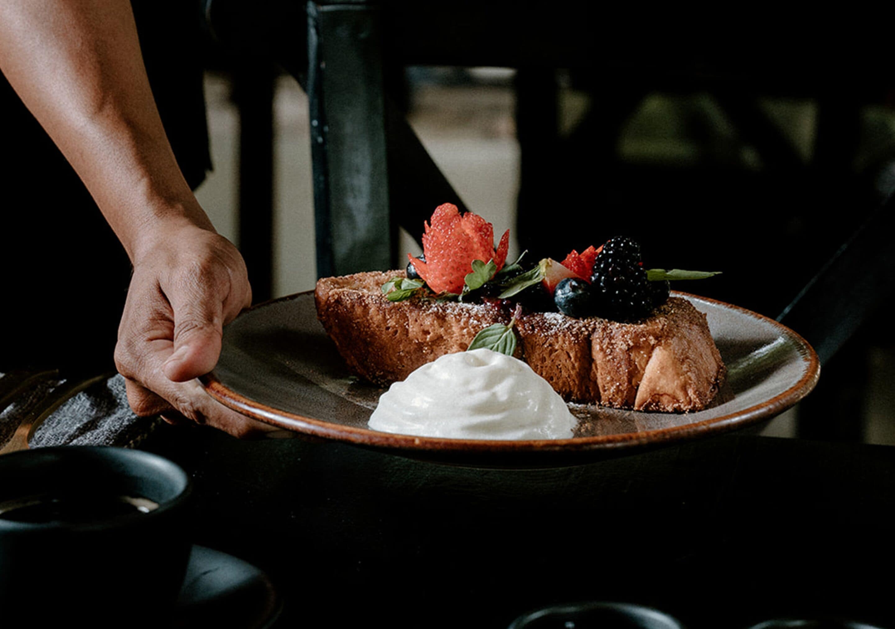 A person holding a plate with two pieces of toast topped with strawberries, blueberries, and a dollop of cream.