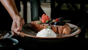 A person holding a plate with two pieces of toast topped with strawberries, blueberries, and a dollop of cream.