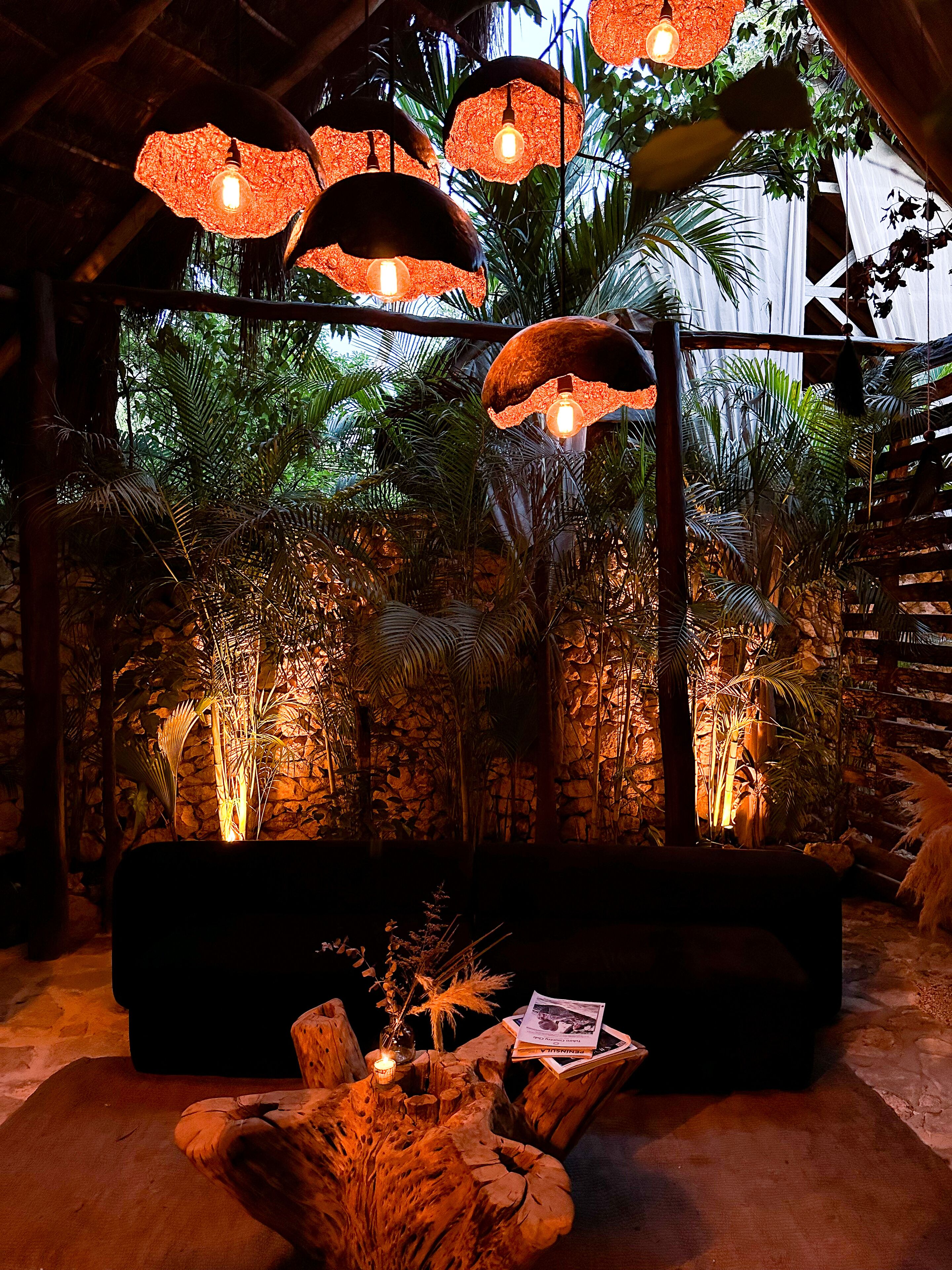 A cozy seating area with a stone wall backdrop, hanging lamps, and lush tropical plants.