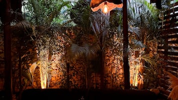 A cozy seating area with a stone wall backdrop, hanging lamps, and lush tropical plants.