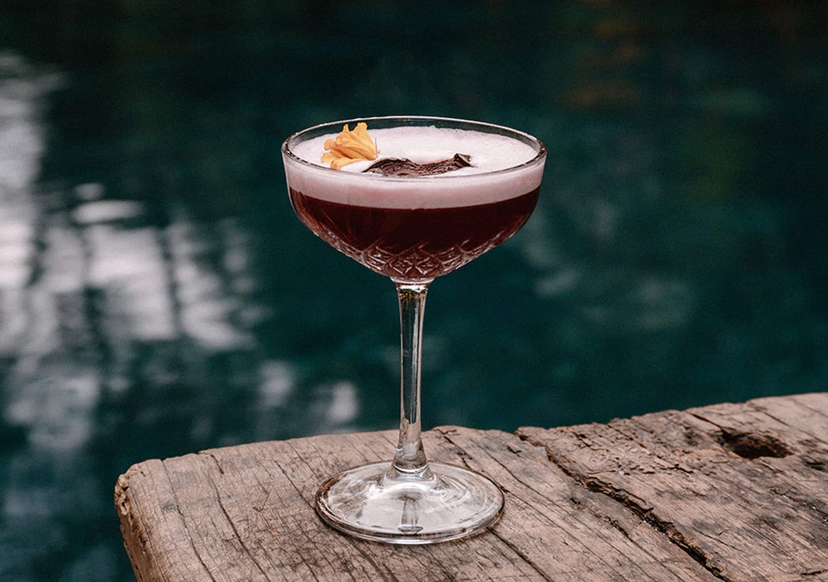 A cocktail in a glass on a wooden surface with a blurred background.